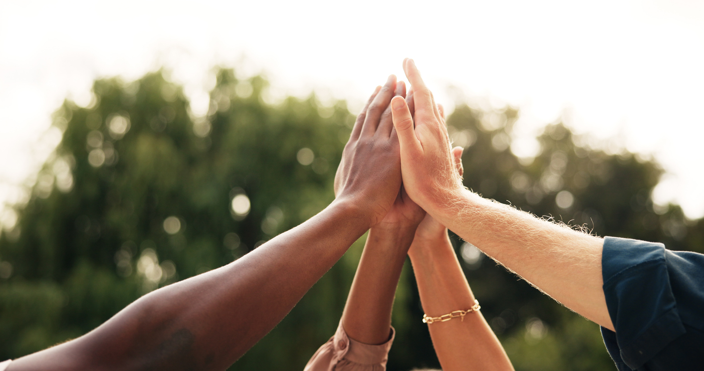 Diverse hands joining in a high-five outdoors, symbolizing teamwork and unity.