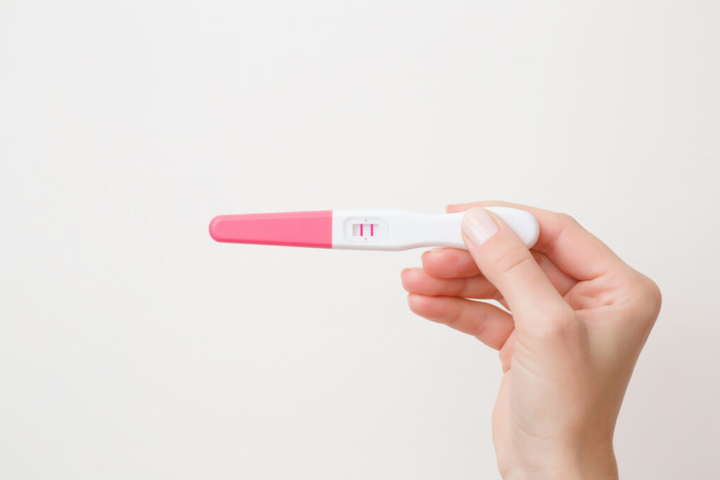 Hand holding a white and pink home pregnancy test showing two pink lines in the result window (positive result).